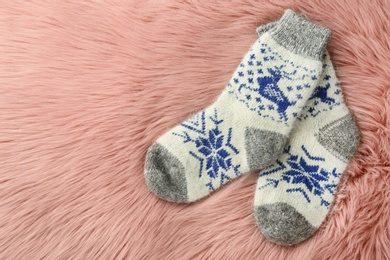 Photo of Knitted socks on pink faux fur, flat lay. Space for text