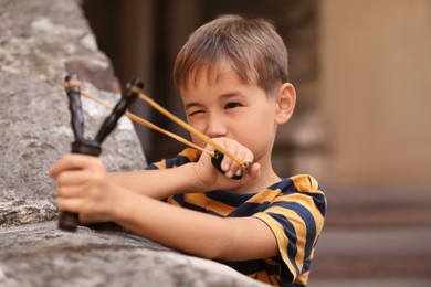 Photo of Cute little boy playing with slingshot outdoors