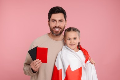 Immigration. Happy man holding passports and his daughter with Canadian flag on pink background