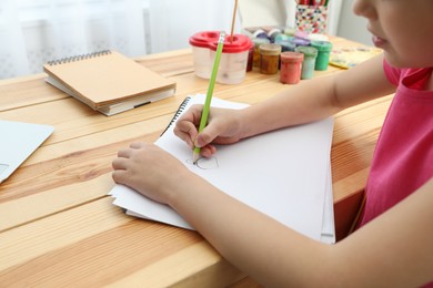 Photo of Little girl drawing on paper with pencil at online lesson indoors, closeup. Distance learning