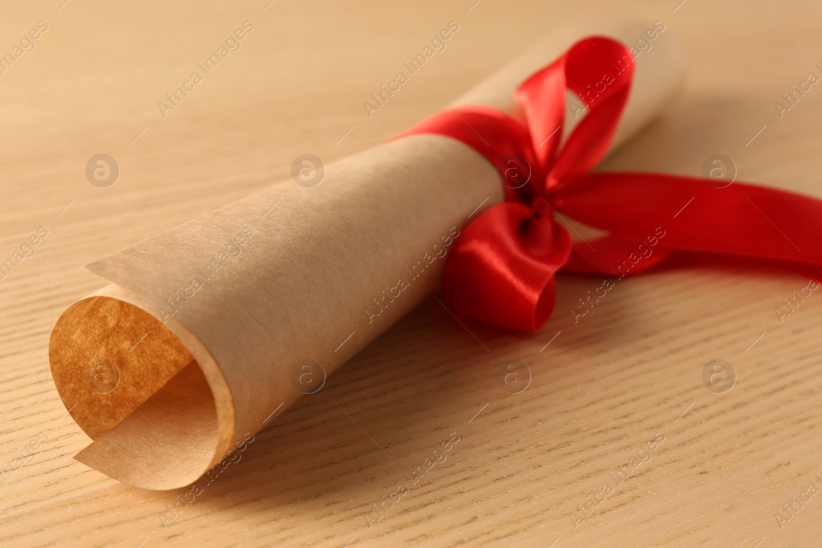 Photo of Graduation diploma tied with red ribbon on wooden table, closeup