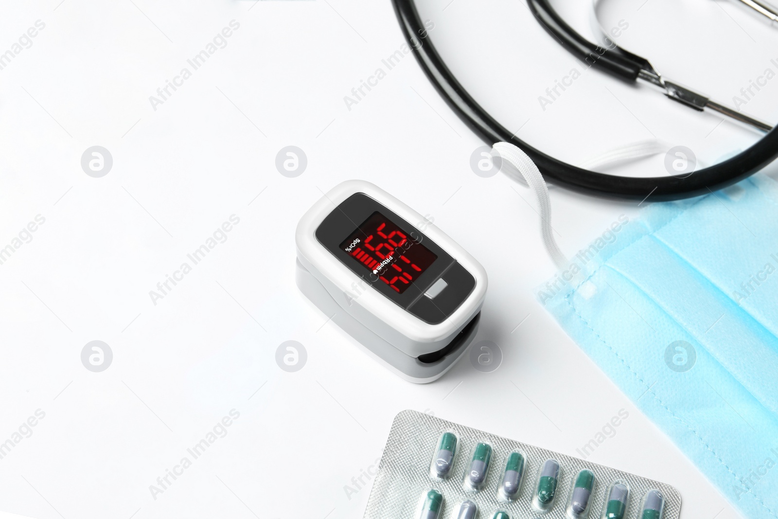 Photo of Composition with fingertip pulse oximeter and pills on white background