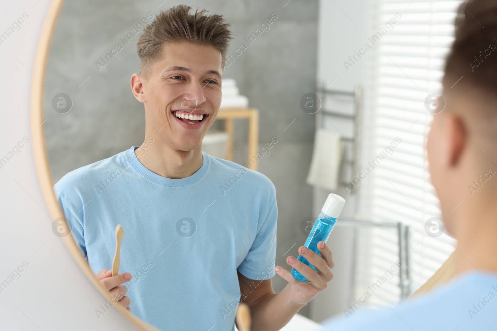 Photo of Young man with mouthwash and toothbrush near mirror in bathroom