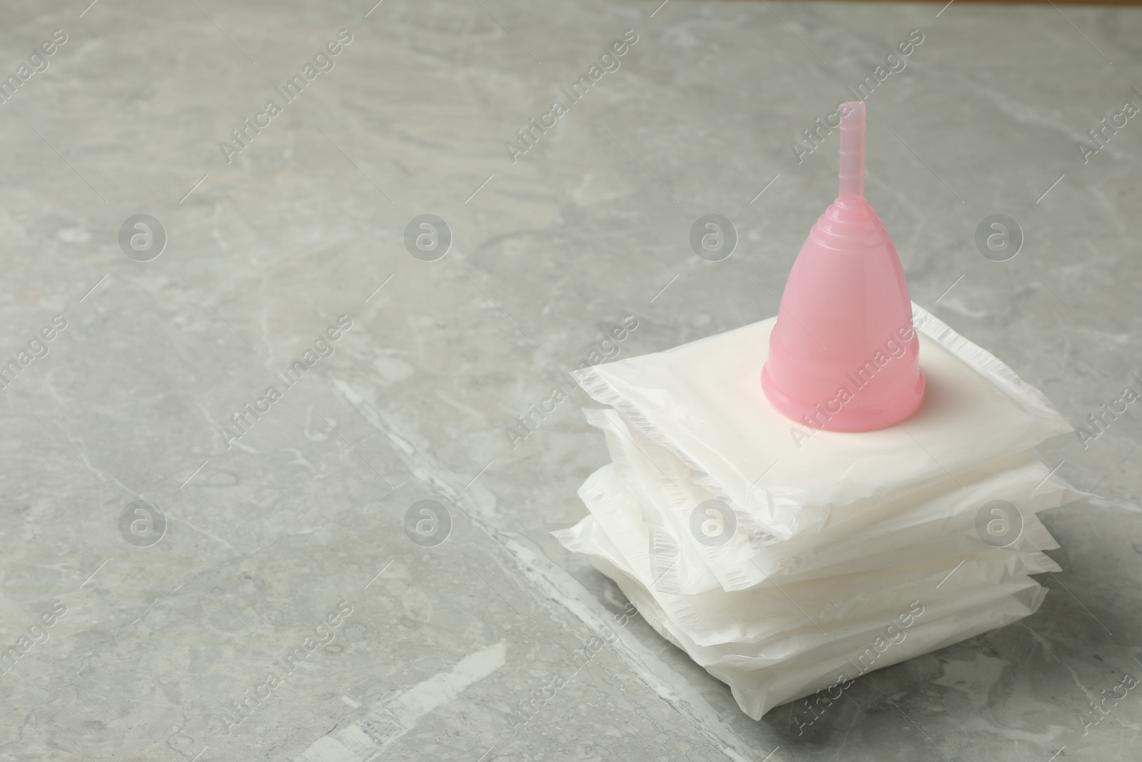 Photo of Menstrual cup and pads on grey table. Space for text