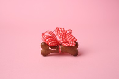 Photo of Bone shaped dog cookie with red bow on pink background