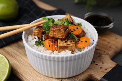 Bowl of rice with fried tofu, broccoli and carrots on wooden board, closeup