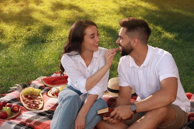 Photo of Lovely couple having picnic on plaid outdoors