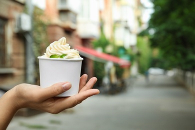 Photo of Woman holding cup with tasty frozen yogurt outdoors, closeup. Space for text