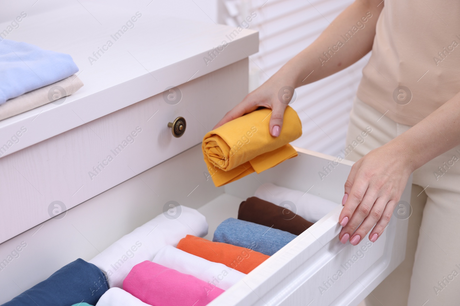 Photo of Woman putting rolled shirt into drawer at home, closeup. Organizing clothes