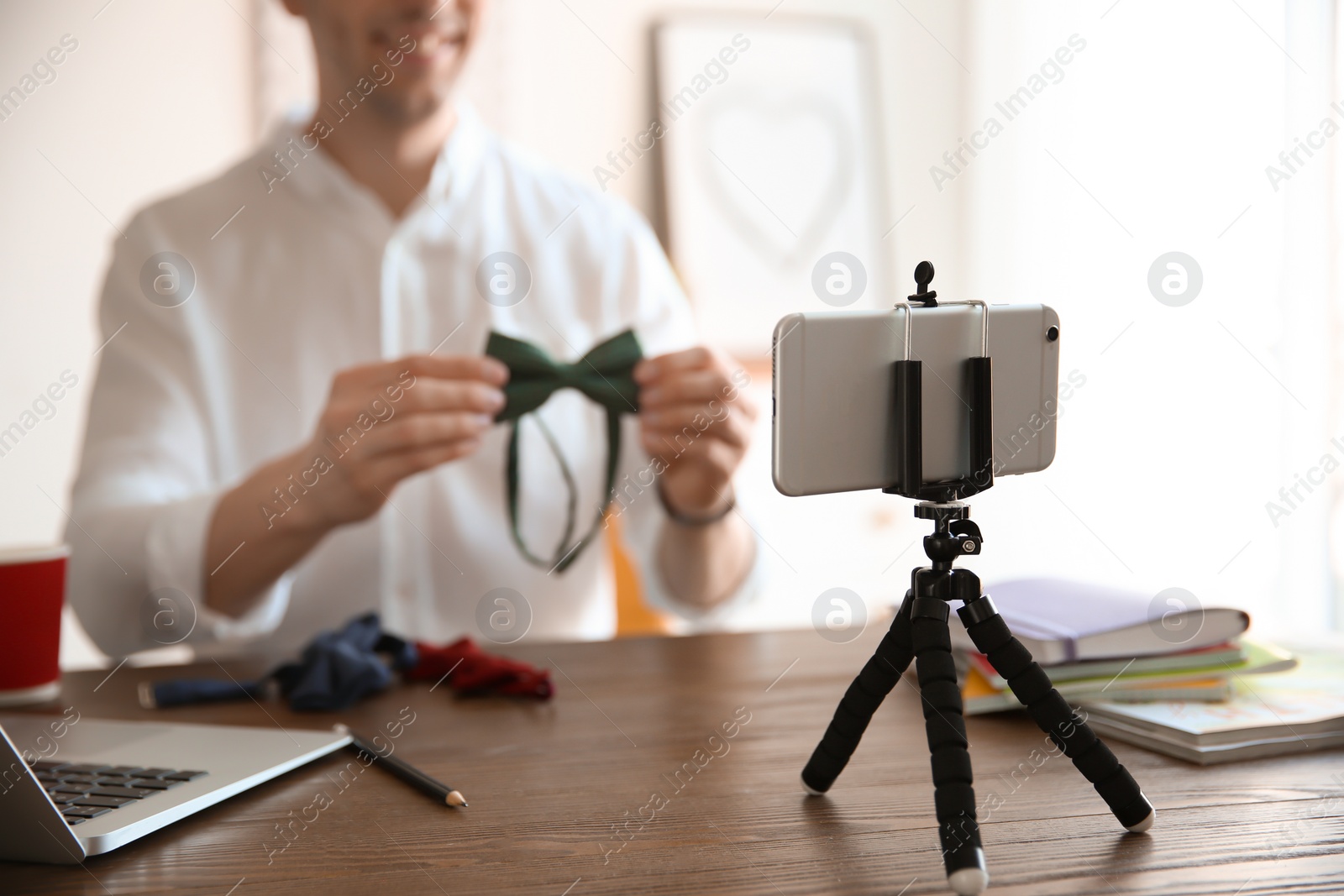 Photo of Young blogger with bow tie recording video at table