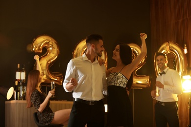 Photo of Young people celebrating New Year in club. Golden 2020 balloons on background