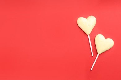 Photo of Chocolate heart shaped lollipops on red background, flat lay. Space for text