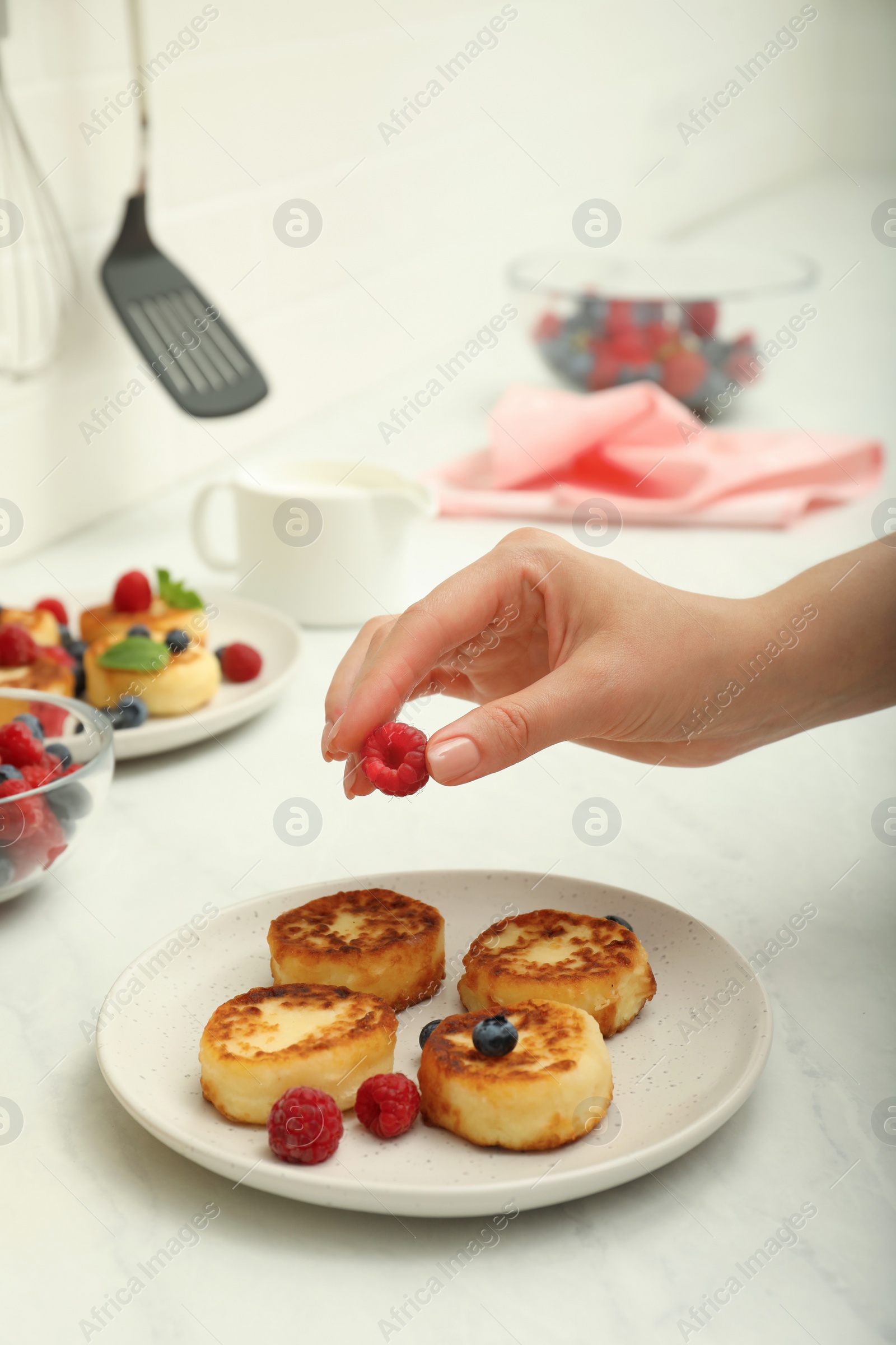 Photo of Woman decorating delicious cottage cheese pancakes with fresh berries at white countertop, closeup