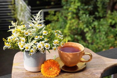 Photo of Cup of delicious chamomile tea and fresh flowers outdoors on sunny day