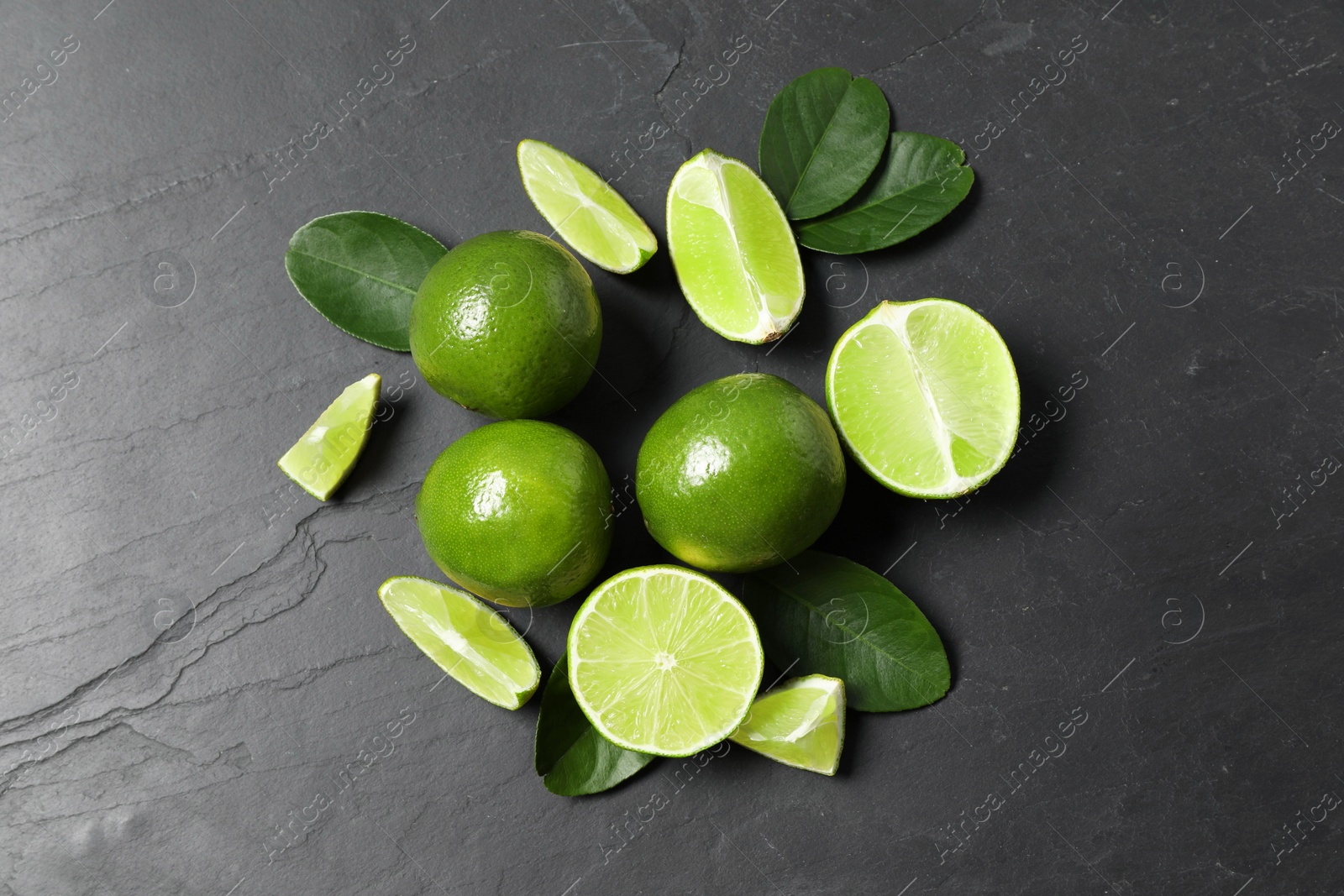 Photo of Fresh ripe limes and leaves on black table, top view