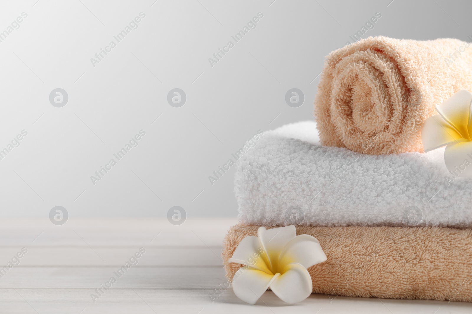 Photo of Closeup view of soft folded towels and plumeria flowers on white wooden table, space for text