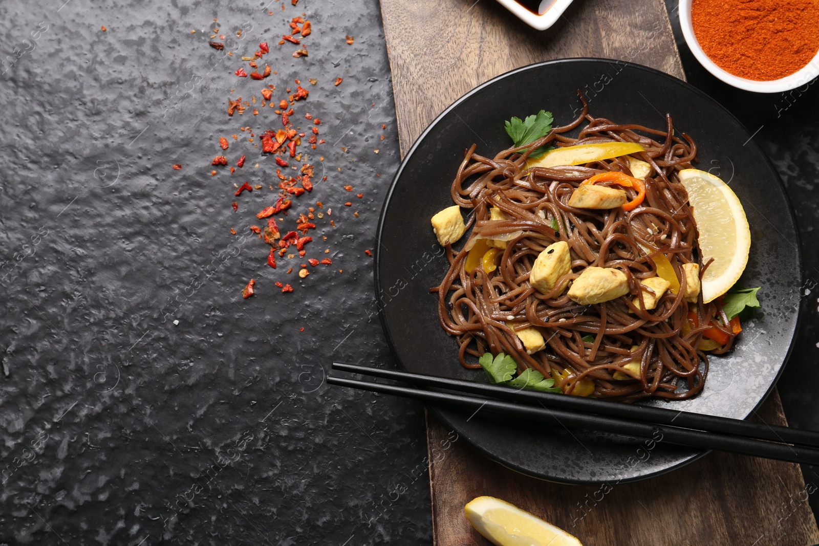 Photo of Stir-fry. Tasty noodles with vegetables and meat served on dark textured table, flat lay. Space for text