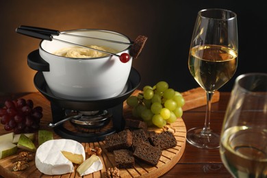 Photo of Forks with pieces of grape, bread, fondue pot with melted cheese, wine and snacks on wooden table, closeup