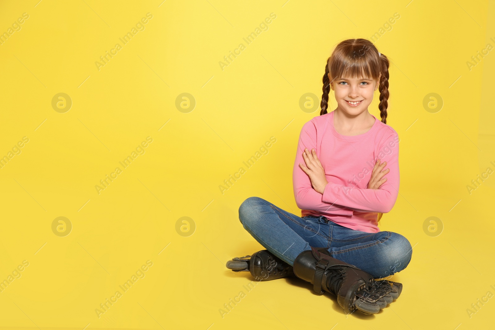 Photo of Girl with inline roller skates sitting on color background. Space for text