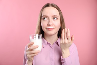 Photo of Cute woman with milk mustache holding glass of tasty dairy drink on pink background