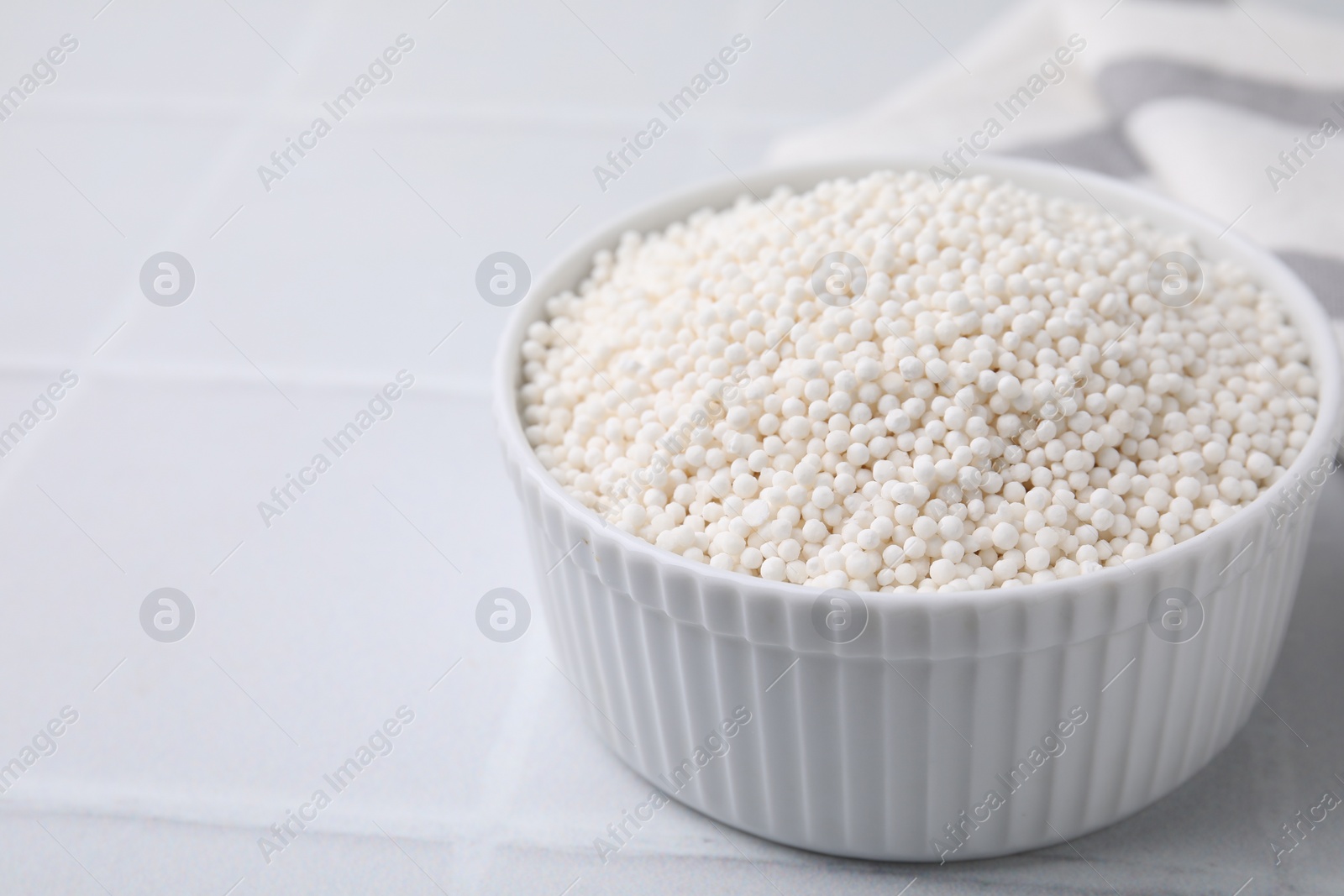 Photo of Tapioca pearls in bowl on white tiled table, closeup. Space for text