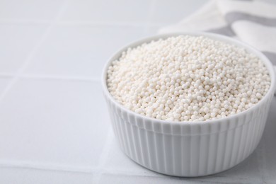 Photo of Tapioca pearls in bowl on white tiled table, closeup. Space for text