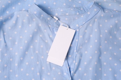 Photo of Blank white tags on light blue shirt with polka dot pattern, top view. Space for text
