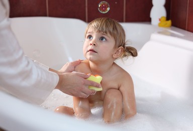 Photo of Mother washing her little daughter with sponge in bathtub, closeup