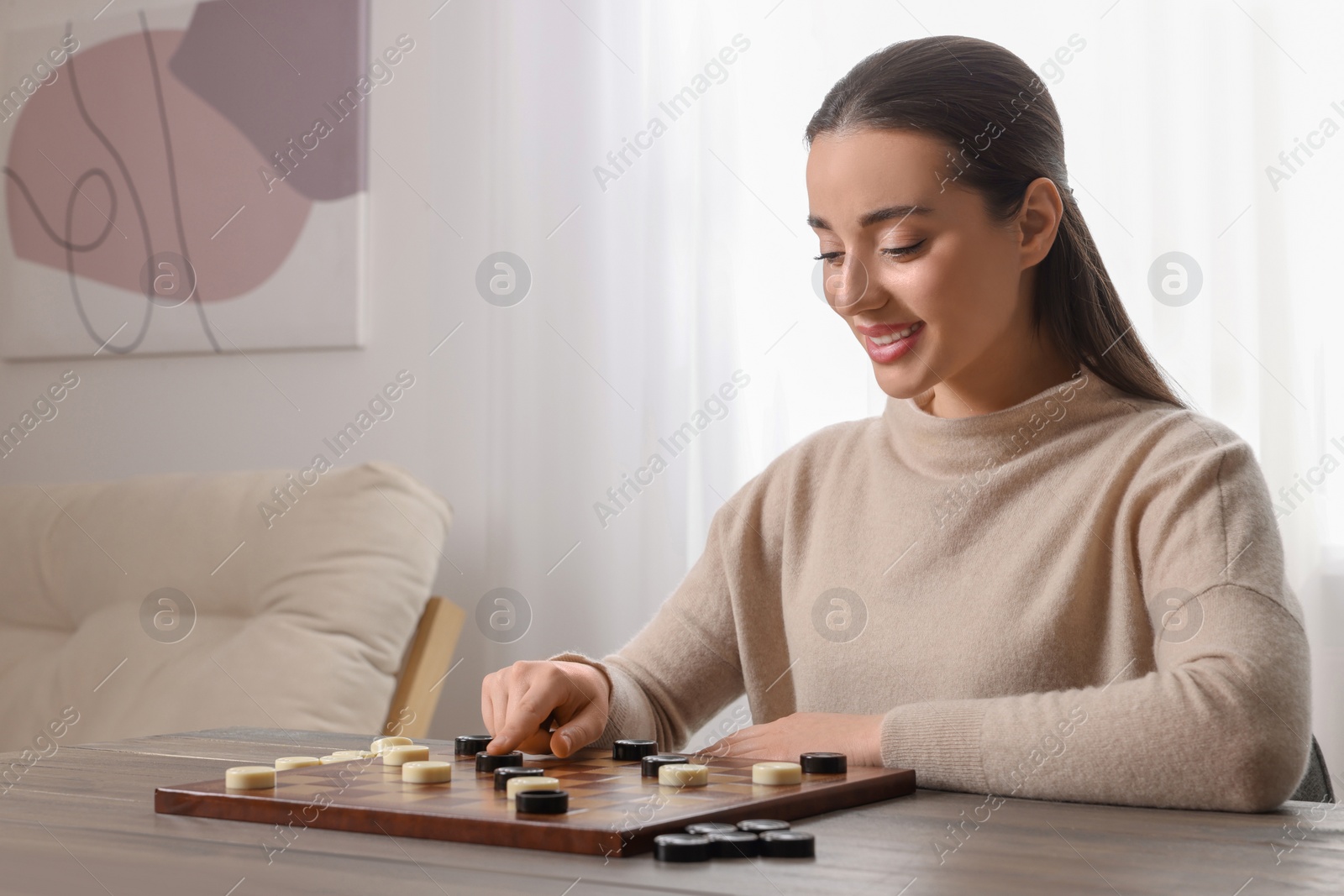 Photo of Playing checkers. Young woman thinking about next move at table in room, space for text