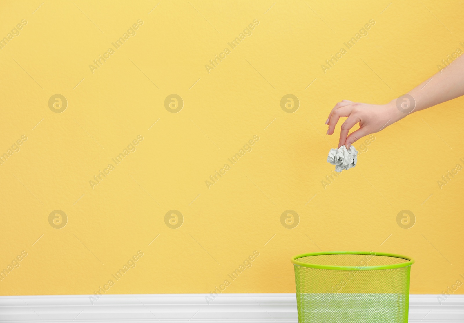 Photo of Woman throwing crumpled paper into metal bin against color background. Space for text