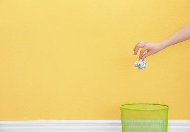 Photo of Woman throwing crumpled paper into metal bin against color background. Space for text