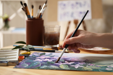 Photo of Woman painting flowers with watercolor at table in workshop, closeup