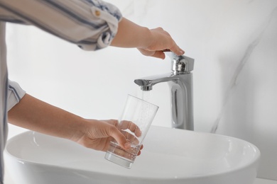 Photo of Woman filling glass with water from faucet over sink, closeup