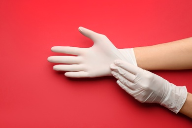 Person putting on medical gloves against red background, closeup of hands