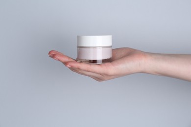 Woman holding jar of cream on grey background, closeup