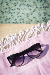 Stylish sunglasses and blanket near outdoor pool on sunny day, above view. Space for text