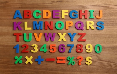 Photo of Plastic magnetic letters, numbers and math symbols on wooden background, top view
