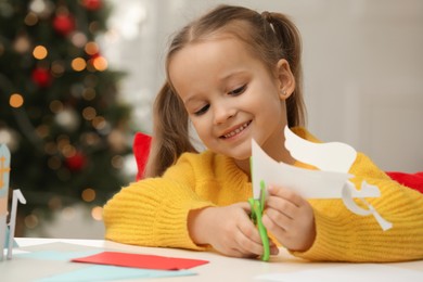 Photo of Cute little girl making paper angel for Saint Nicholas day at home