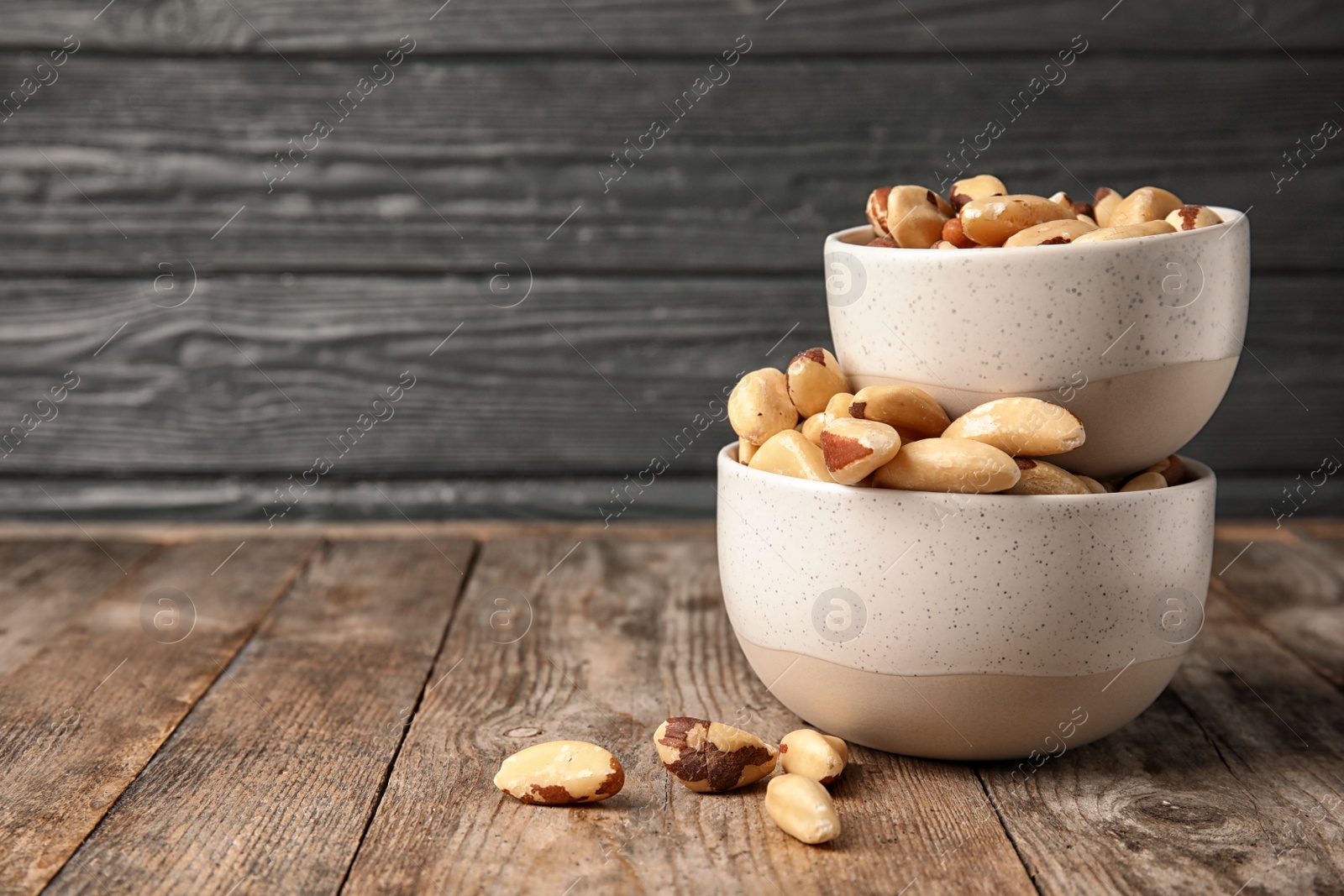 Photo of Bowls with tasty Brazil nuts on wooden table. Space for text