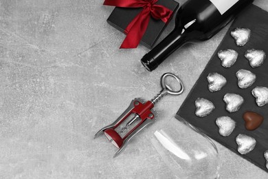 Photo of Bottle of red wine, glass, heart shaped chocolate candies, corkscrew and gift box on light grey textured table, flat lay. Space for text