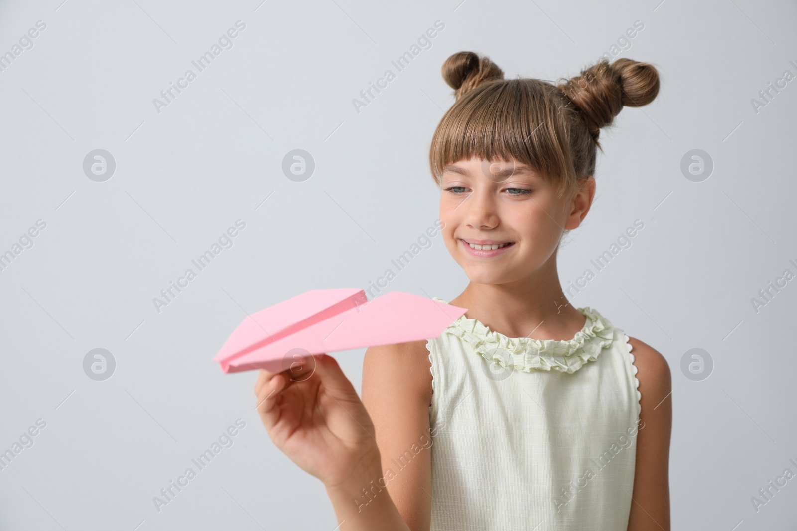 Photo of Cute little girl playing with paper plane on light grey background