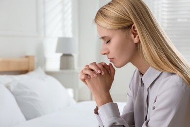 Religious young woman praying in bedroom. Space for text