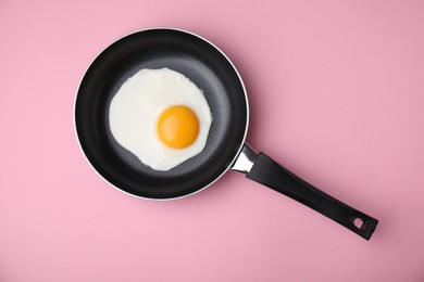Photo of Tasty fried egg in pan on pink background, top view