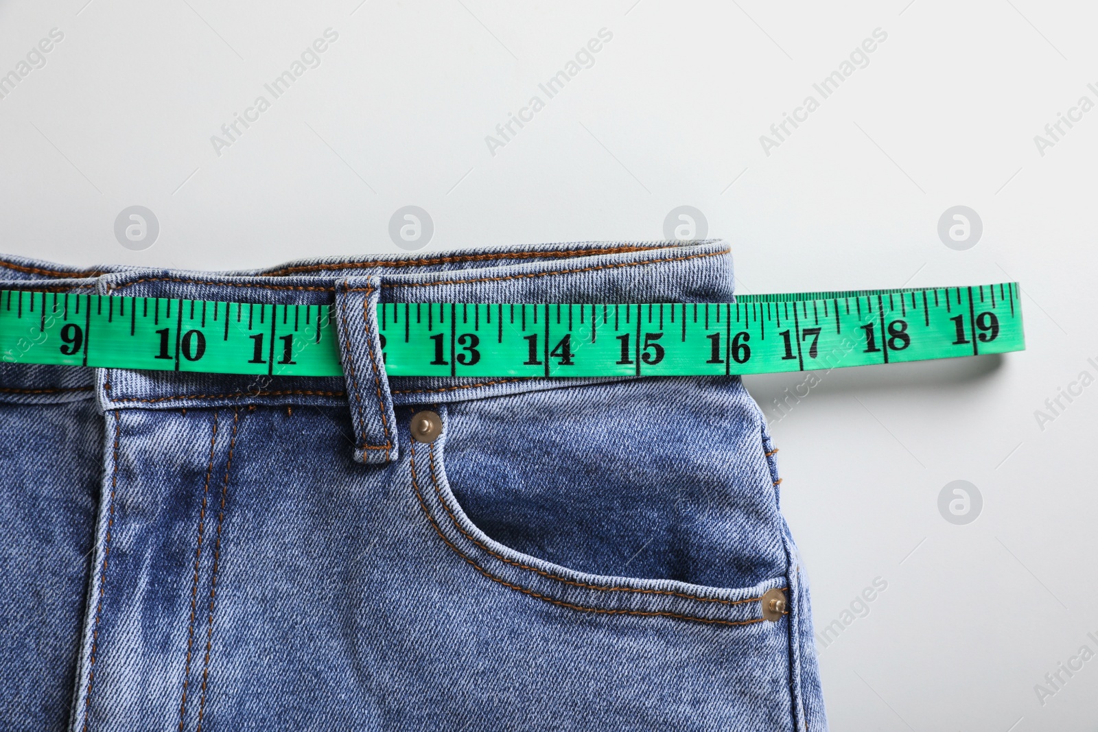 Photo of Jeans with measuring tape on light grey background, top view. Weight loss concept