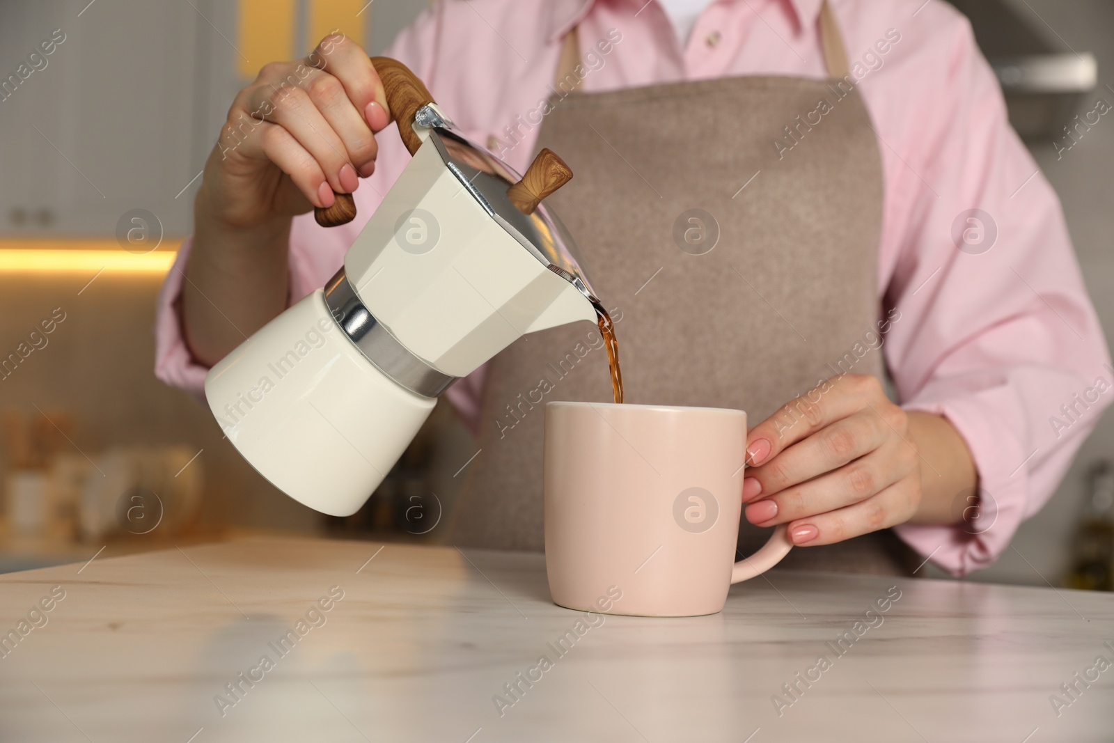 Photo of Woman pouring aromatic coffee from moka pot into cup at white marble table, closeup