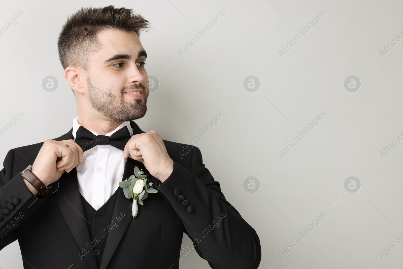 Photo of Handsome young groom with boutonniere on light grey background, space for text. Wedding accessory