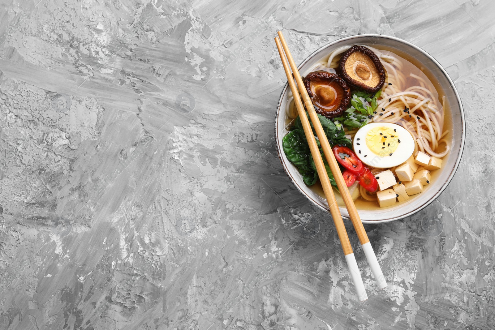 Photo of Delicious vegetarian ramen served on grey table, top view with space for text. Noodle soup