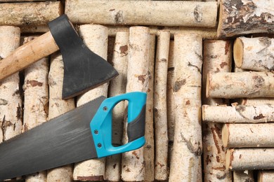 Photo of Saw with light blue handle and axe on firewood, flat lay