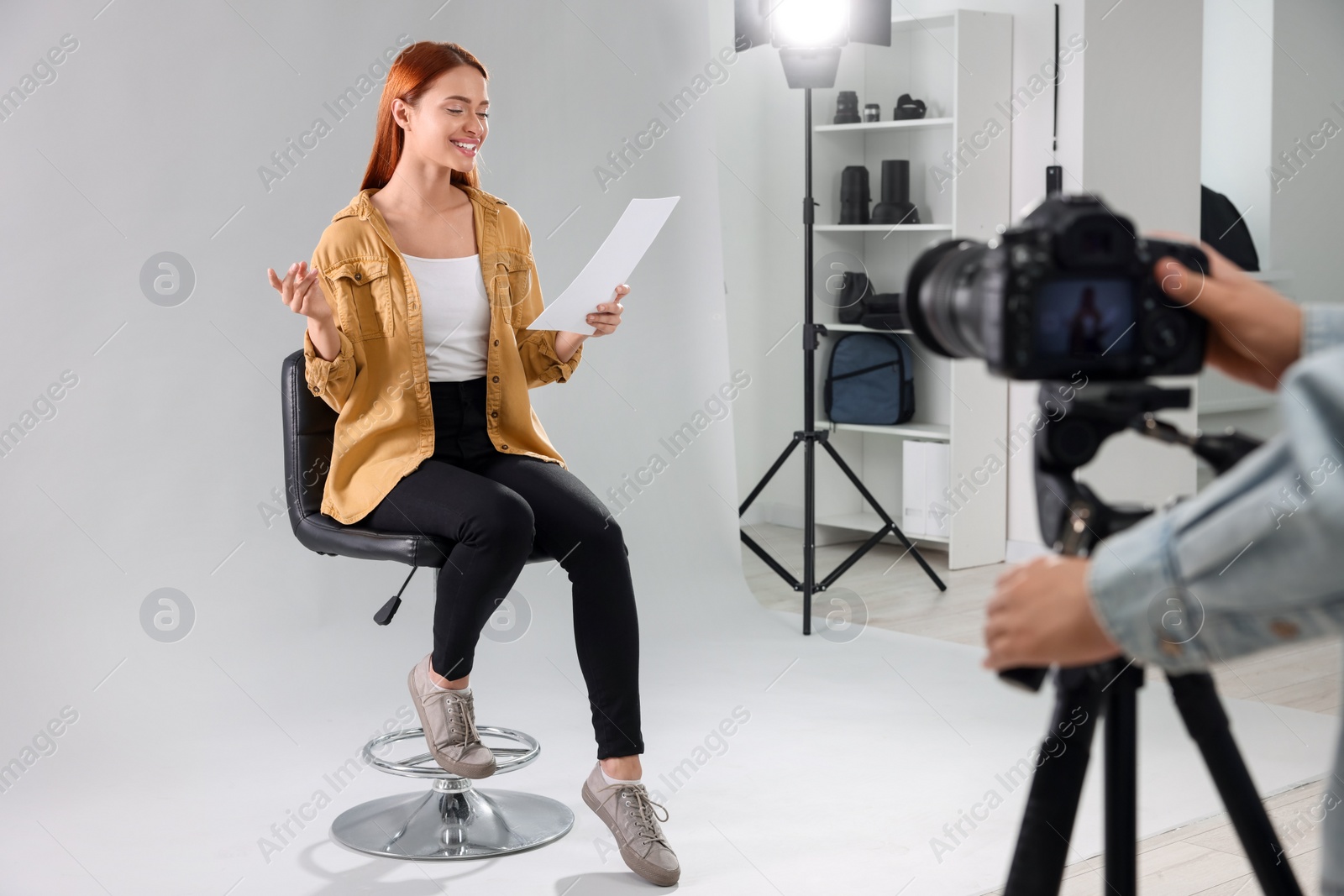 Photo of Casting call. Woman with script performing while camera operator filming her against light grey background in studio