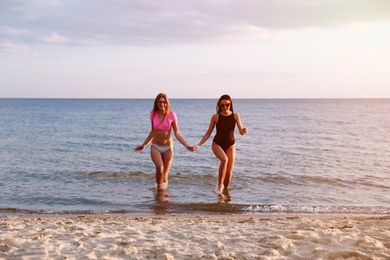 Young woman in bikini with girlfriend on beach. Lovely couple